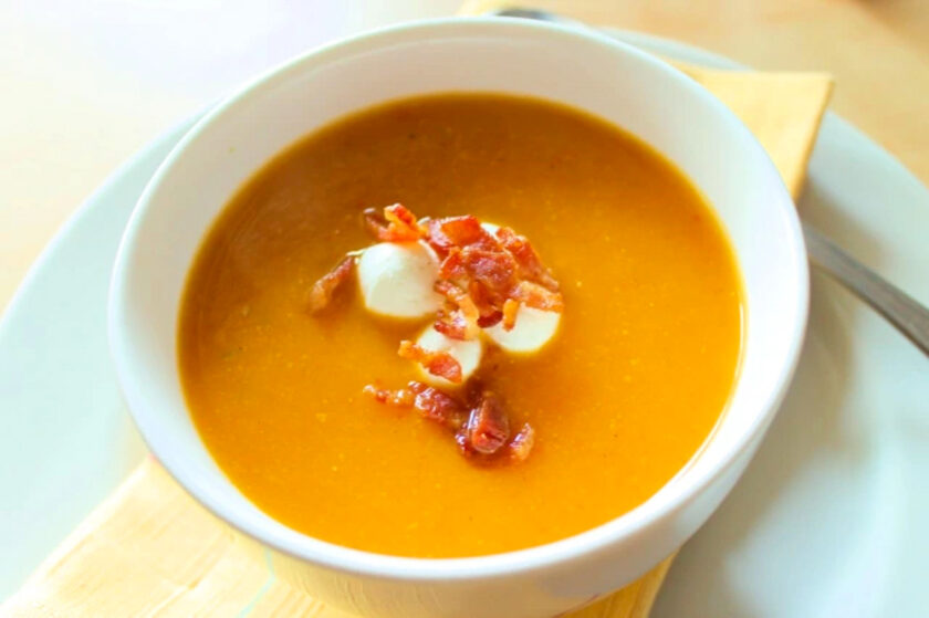 A bowl of soup with bacon on top.