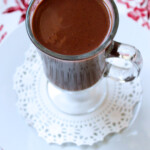 Una taza de chocolate caliente sobre un plato con una blonda.
