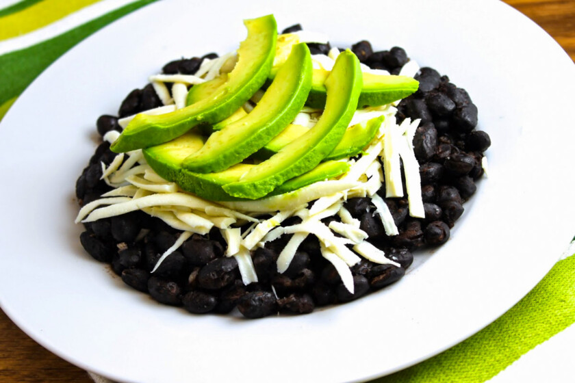 A plate with black beans, white cheese, and avocado on it.