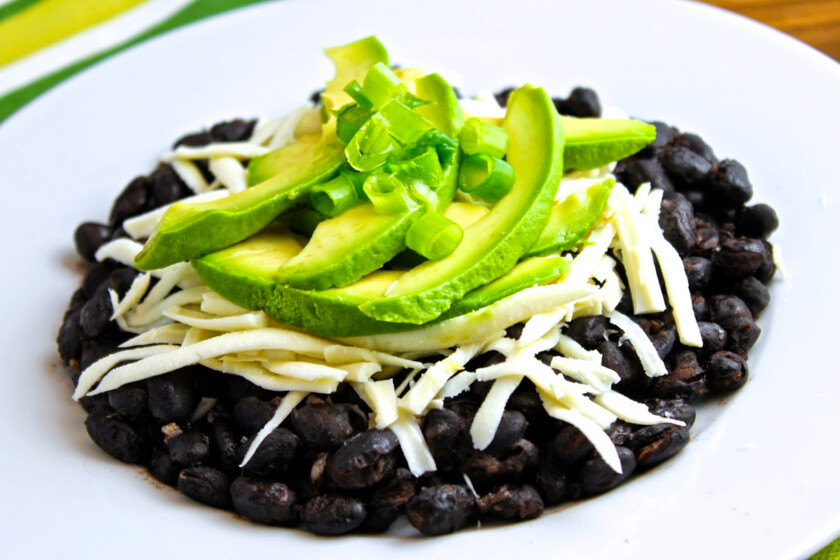 Un plato de caraotas negras refritas con aguacate y queso.