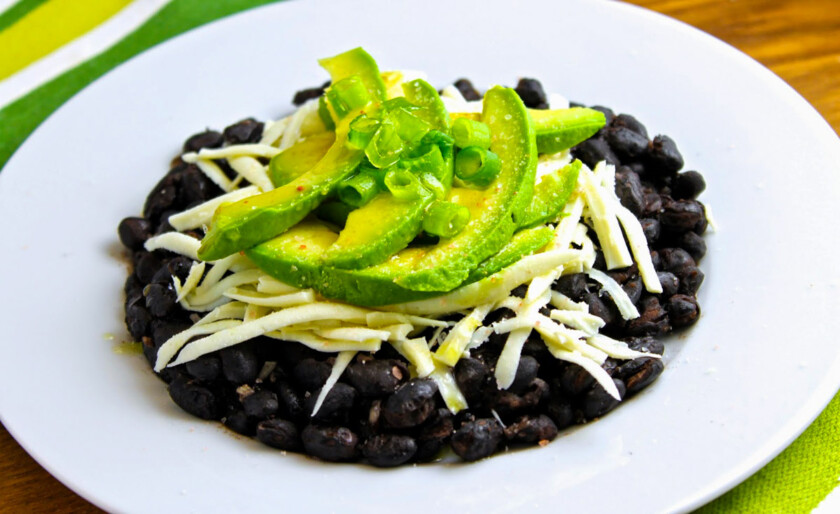 A plate of black beans with avocado and cheese.