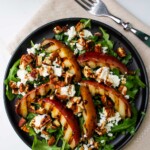 A black plate with a salad with grilled pears and goat cheese.