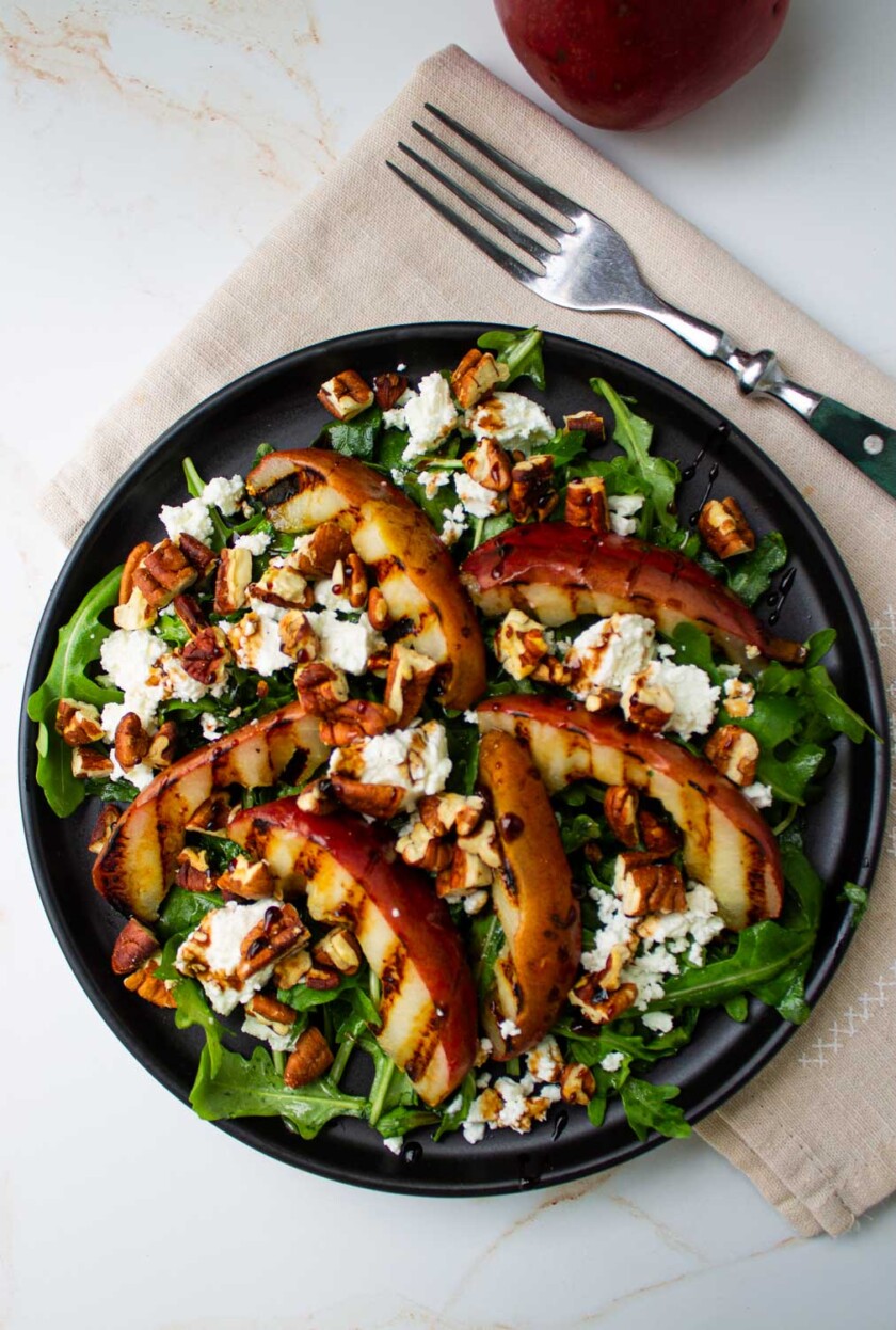 A black plate with a salad with grilled pears and goat cheese.
