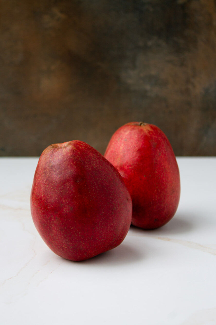 Two red pears on a white marble surface.