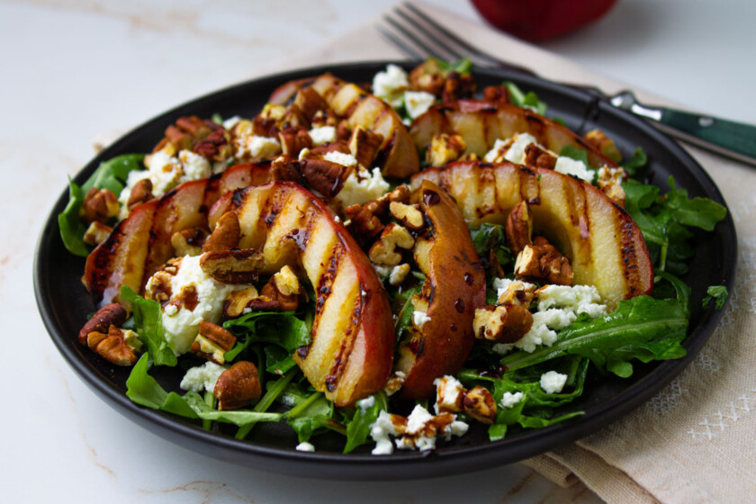 A black plate with a salad with grilled pears and goat cheese.