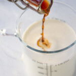 A person pouring vanilla into a measuring cup with heavy cream.