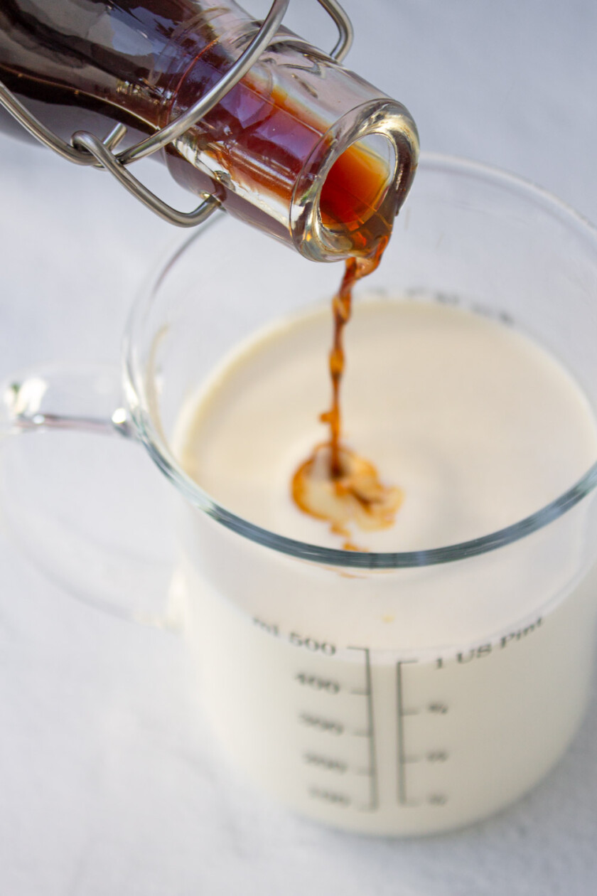 A person pouring vanilla into a measuring cup with heavy cream.