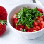 Diced strawberries with chopped basiol on a white bowl.