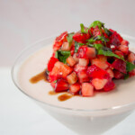 A martini glass with strawberry panna cotta with fresh strawberry and basil on top.