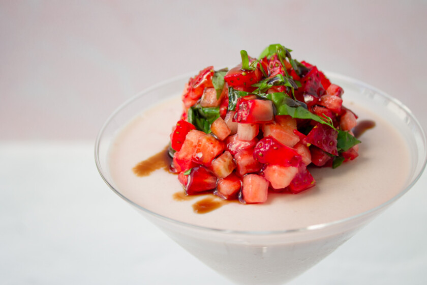 A martini glass with strawberry panna cotta with fresh strawberry and basil on top.