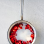 Strawberries with sugar in a metal pan on a white surface.