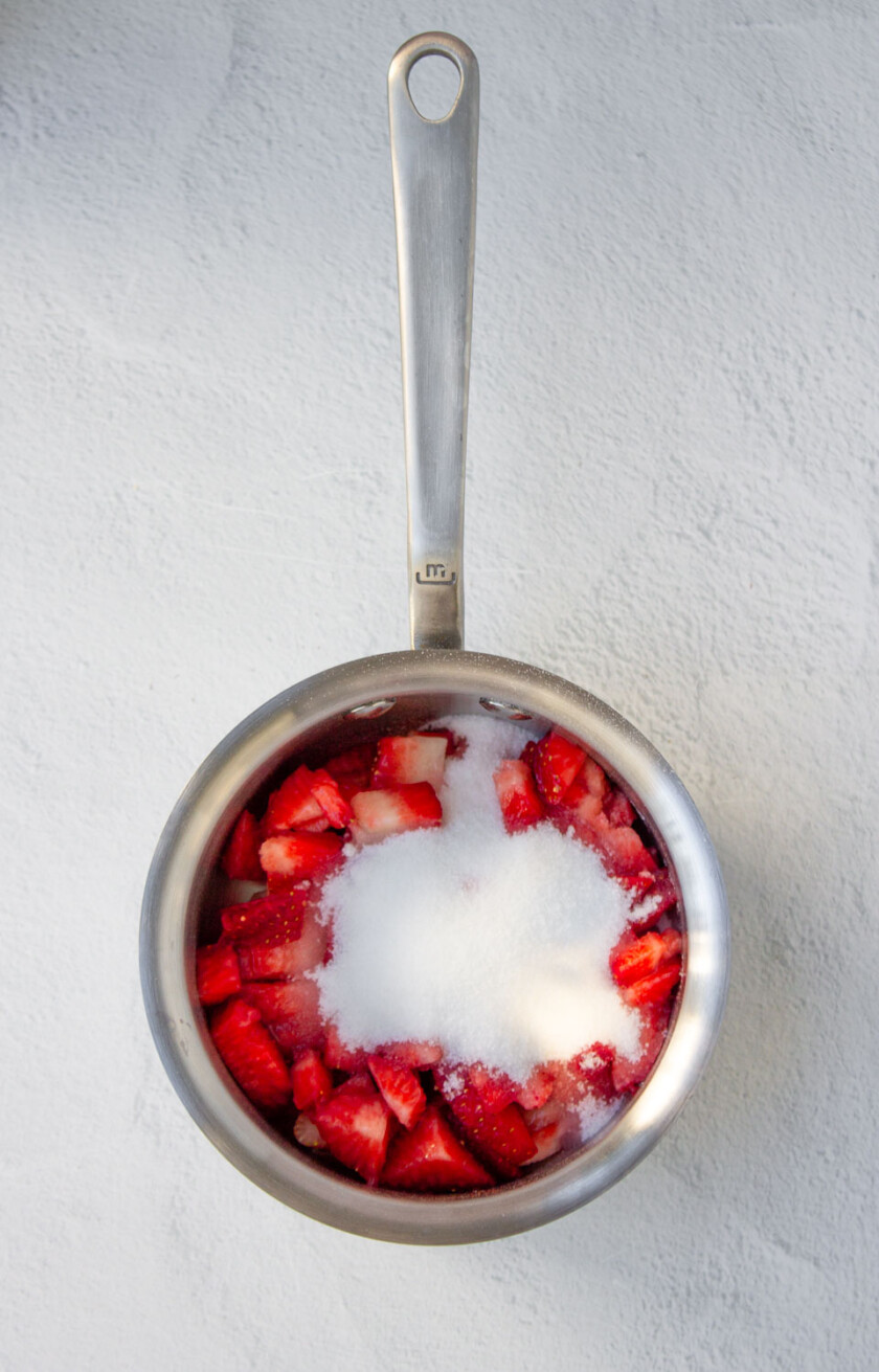 Strawberries with sugar in a metal pan on a white surface.