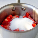 Una olla de acero inoxidable llena de fresas y azúcar.