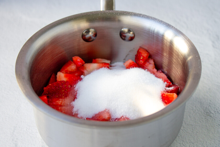 Una olla de acero inoxidable llena de fresas y azúcar.