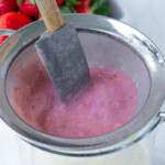 A strainer filled with a strawberry mixture and a spatula.