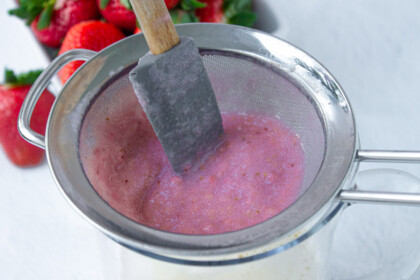 A strainer filled with a strawberry mixture and a spatula.