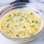 A bowl of creamy leek soup on a marble surface with a wooden and rubber statula.