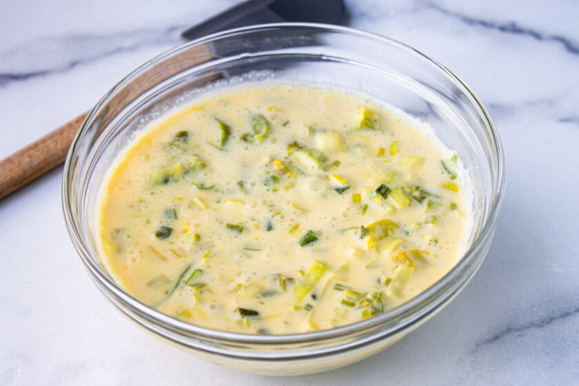 A bowl of creamy leek soup on a marble surface with a wooden and rubber spatula.