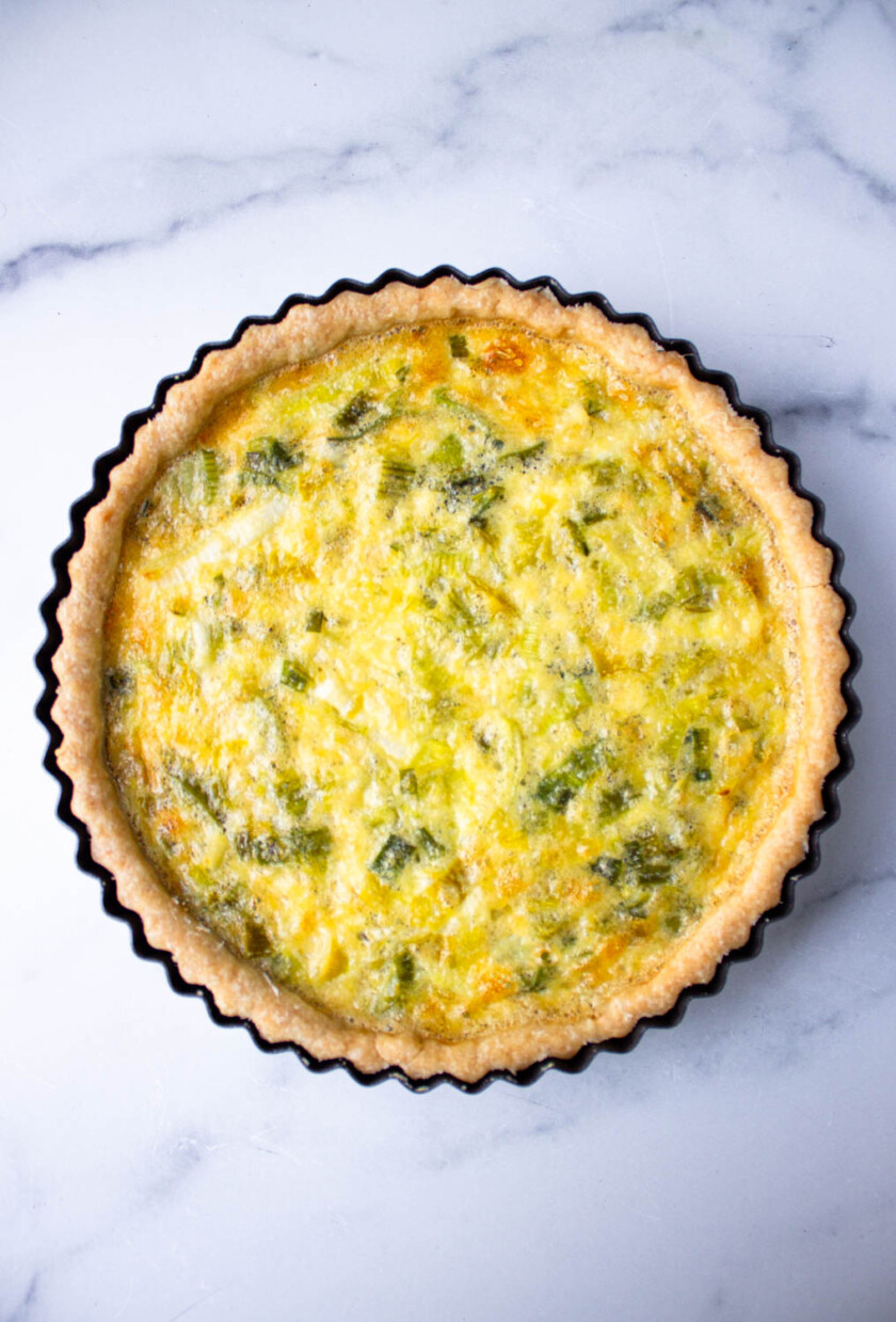 Una quiche dorada de ajo porro, apoyada sobre una superficie de mármol.