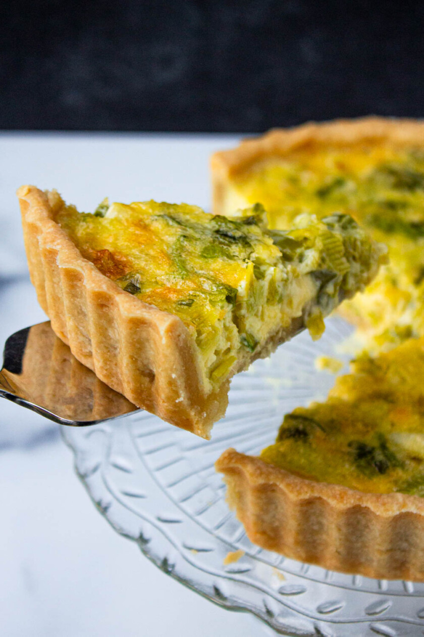 Una porción de quiche con una corteza hojaldrada se levanta con una espátula .