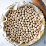 Unbaked pie crust lined with parchment paper and filled with pie weights, ready for blind baking.