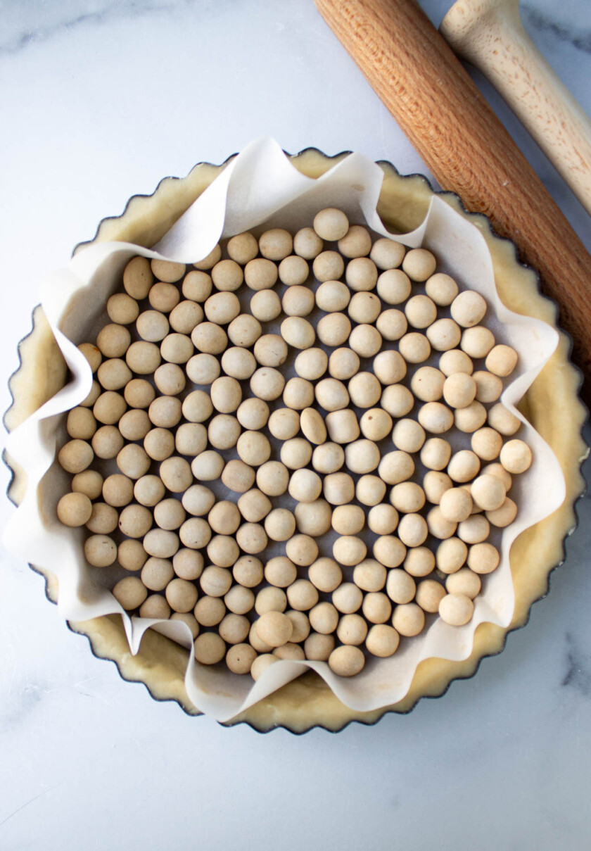 Masa de tarta sin hornear, forrada con pergamino y rellena con pesas para tarta, lista para hornear.