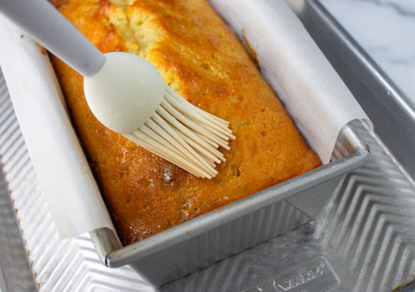 Barnizado de un ponqué con almíbar de limón. El ponqué está recién salido del horno, ennun molde metálico sobre una bandeja de aluminio.