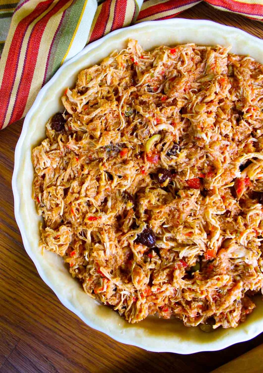 Un pastel con pollo aun sin hornear sobre en una mesa a un mantel a rayas.
