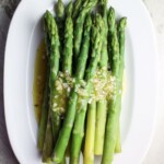 An oval white dish with green asparagus with shallots vinaigrette.