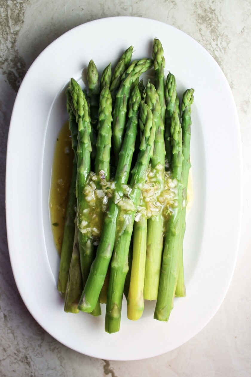 An oval white dish with green asparagus with shallots vinaigrette.