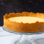 Una tarta de lima clásica sobre un pedestal de cristal, con un relleno suave y cremoso y una corteza de miga de color marrón dorado, sobre un fondo oscuro.