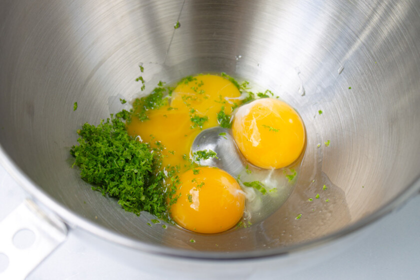 Raw eggs with lime zest in a stainless steel mixing bowl.