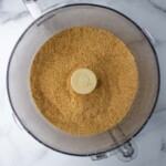 Ground spices in a food processor bowl on a sparkling marble surface.