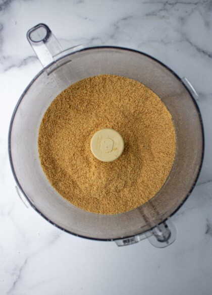 Ground spices in a food processor bowl on a sparkling marble surface.