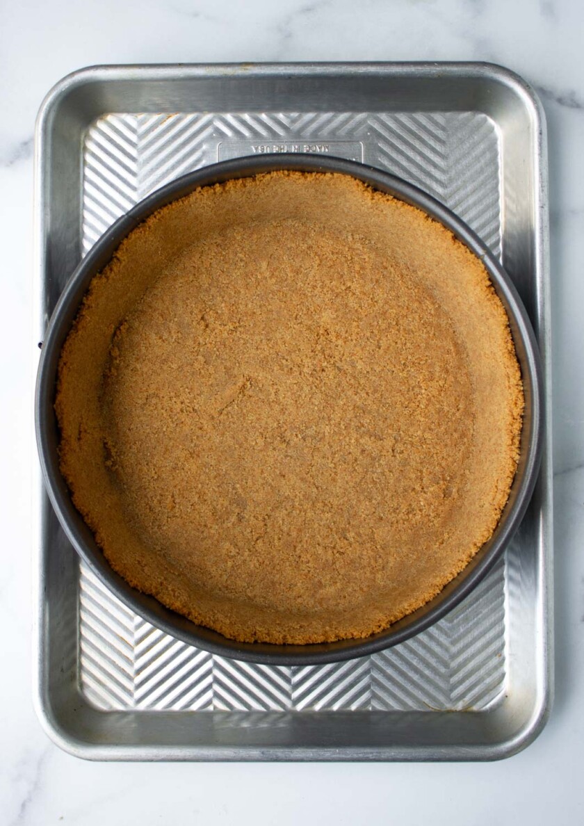 A graham cracker crust in a round pie dish, placed on a metal baking tray.