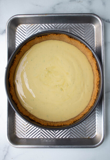 Una tarta de lima con relleno suave y corteza dorada, colocada en una bandeja de metal sobre una superficie de mármol.