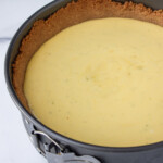 Una tarta de queso recién horneada en un molde desmontable con una corteza dorada de galleta Graham, colocada sobre una superficie de mármol.