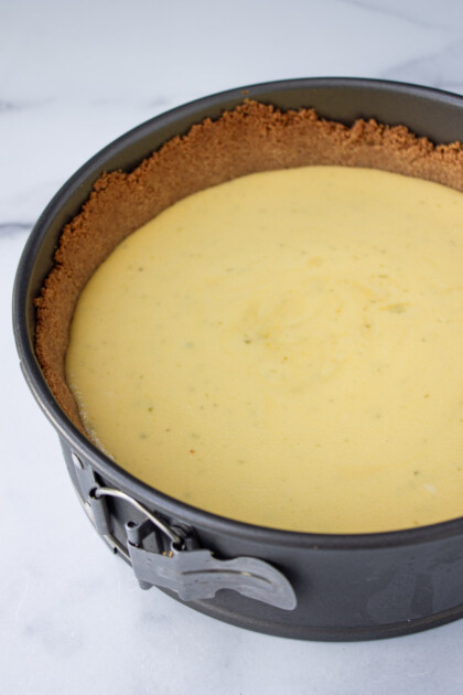 Una tarta de queso recién horneada en un molde desmontable con una corteza dorada de galleta Graham, colocada sobre una superficie de mármol.