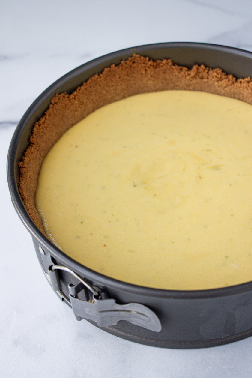 A freshly made key lime pie with a golden crust in a black springform pan on a white marble surface.