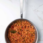 Sartén de acero inoxidable que contiene un guiso de atún con verduras, rsobre una superficie de mármol.