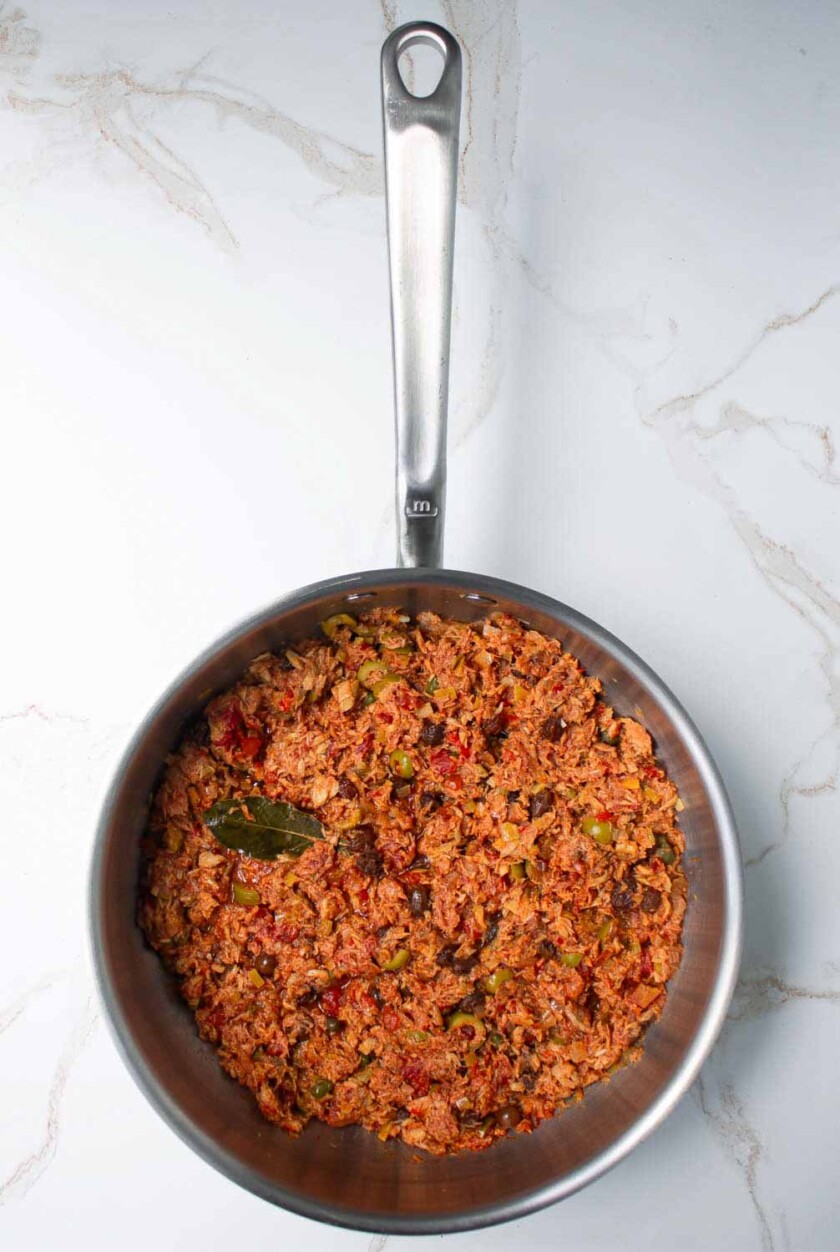 Sartén de acero inoxidable que contiene un guiso de atún con verduras, rsobre una superficie de mármol.