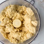 Mezcla de masa quebrada en un procesador de alimentos sobre una encimera de mármol.