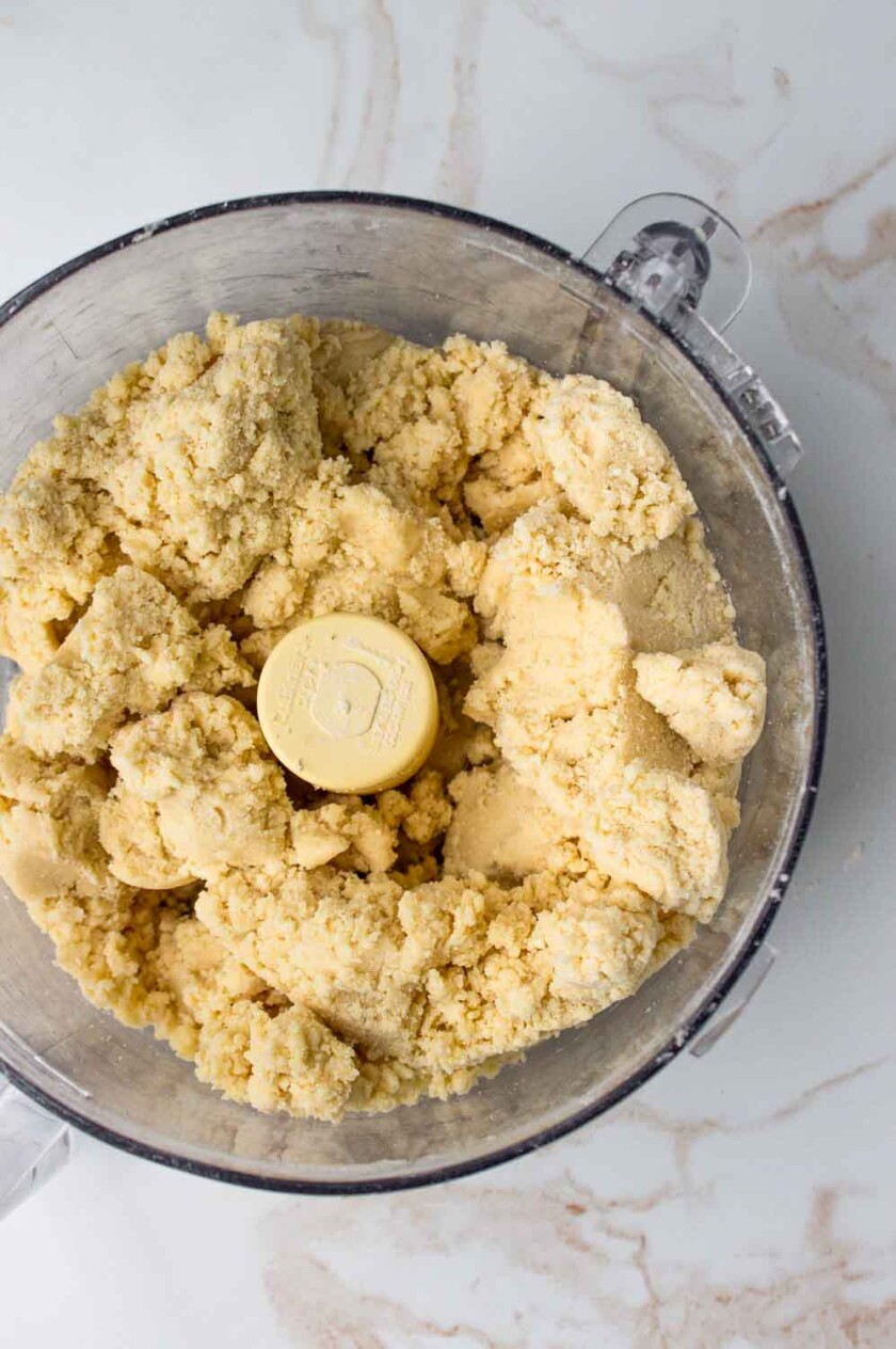 Mezcla de masa quebrada en un procesador de alimentos sobre una encimera de mármol.