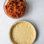 Un tazón de relleno de guiso de atún junto a una base de pastel sin hornear sobre una superficie de mármol.