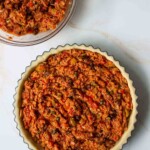 Vista aérea de un relleno de pastel de atún en un molde para tarta, junto a un tazón con relleno adicional. la mezcla parece densa con trozos visibles de verduras.