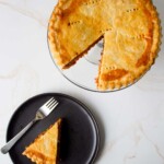Un pastel de polvorosa de atún entero al que se le ha quitado una rebanada, colocado sobre un plato negro con un tenedor sobre una superficie de mármol.