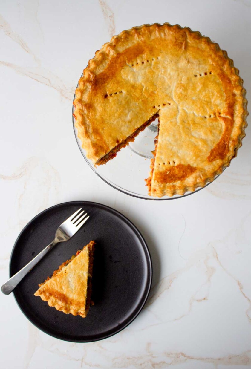 Un pastel de polvorosa de atún entero al que se le ha quitado una rebanada, colocado sobre un plato negro con un tenedor sobre una superficie de mármol.