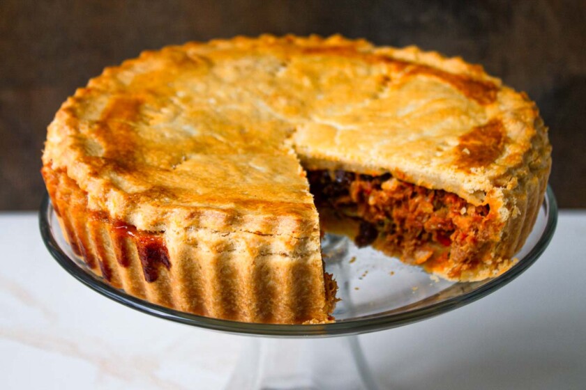Un pastel de polvorosa de atún, dorado, con una porción cortada que deja al descubierto un sabroso relleno, servido en un plato de vidrio transparente.