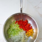 Sartén de acero inoxidable con pimientos y cebollas verdes, amarillos y rojos finamente picados, dispuestos en secciones de colores separados sobre una encimera de mármol.