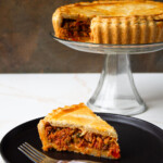 Tuna Polvorosa on a glass cake plate and a piece of the same savory pie on a black dish with a fork.